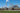 Power plant with large smokestacks releasing steam and smoke, and trains passing by.