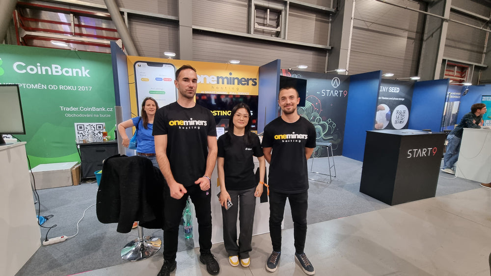 Three people in black t-shirts standing in front of various booths at an event.