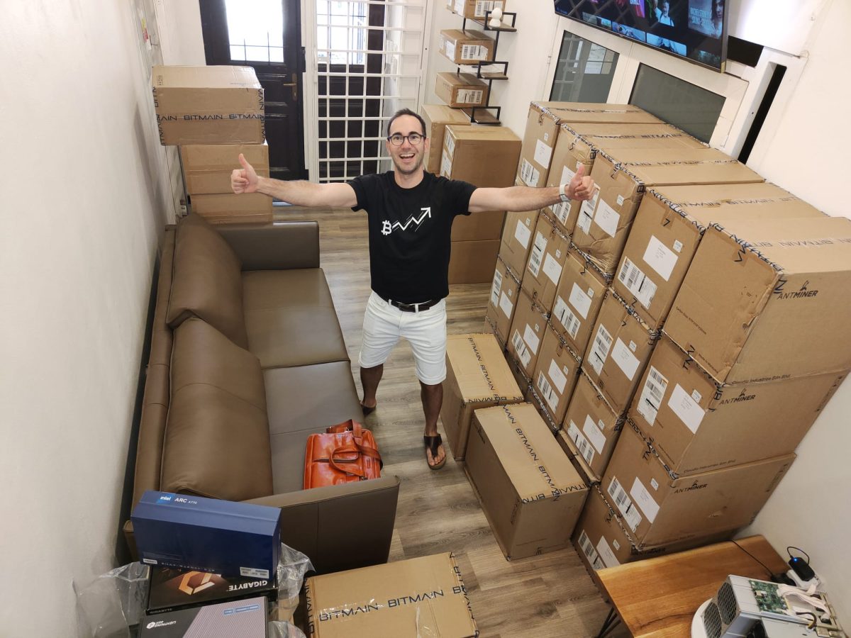 PCPrahaの廊下に立つMichal。周囲にはASICマイナーの箱が積まれている