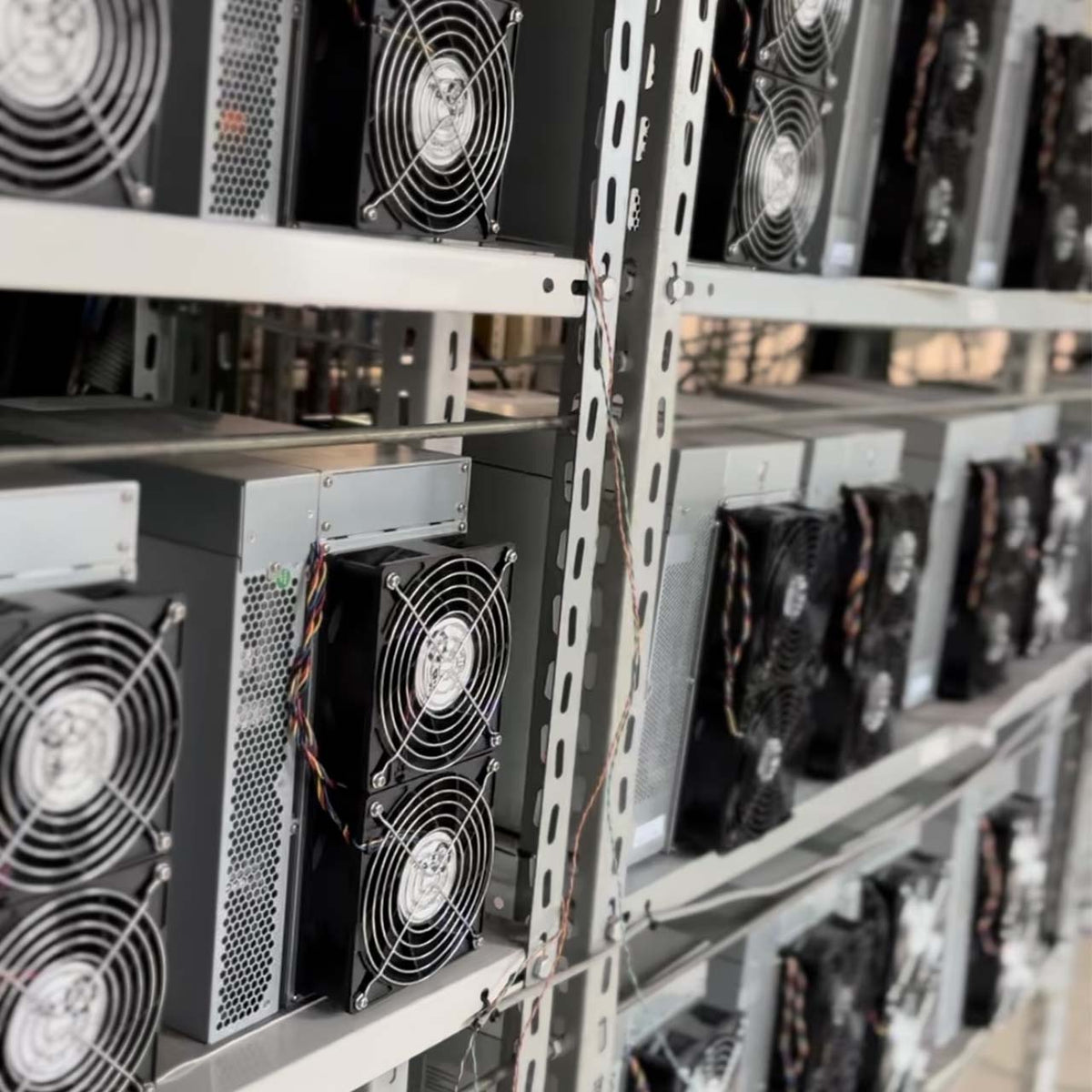 Close-up of multiple cryptocurrency mining machines on shelves with visible cooling fans and wiring.