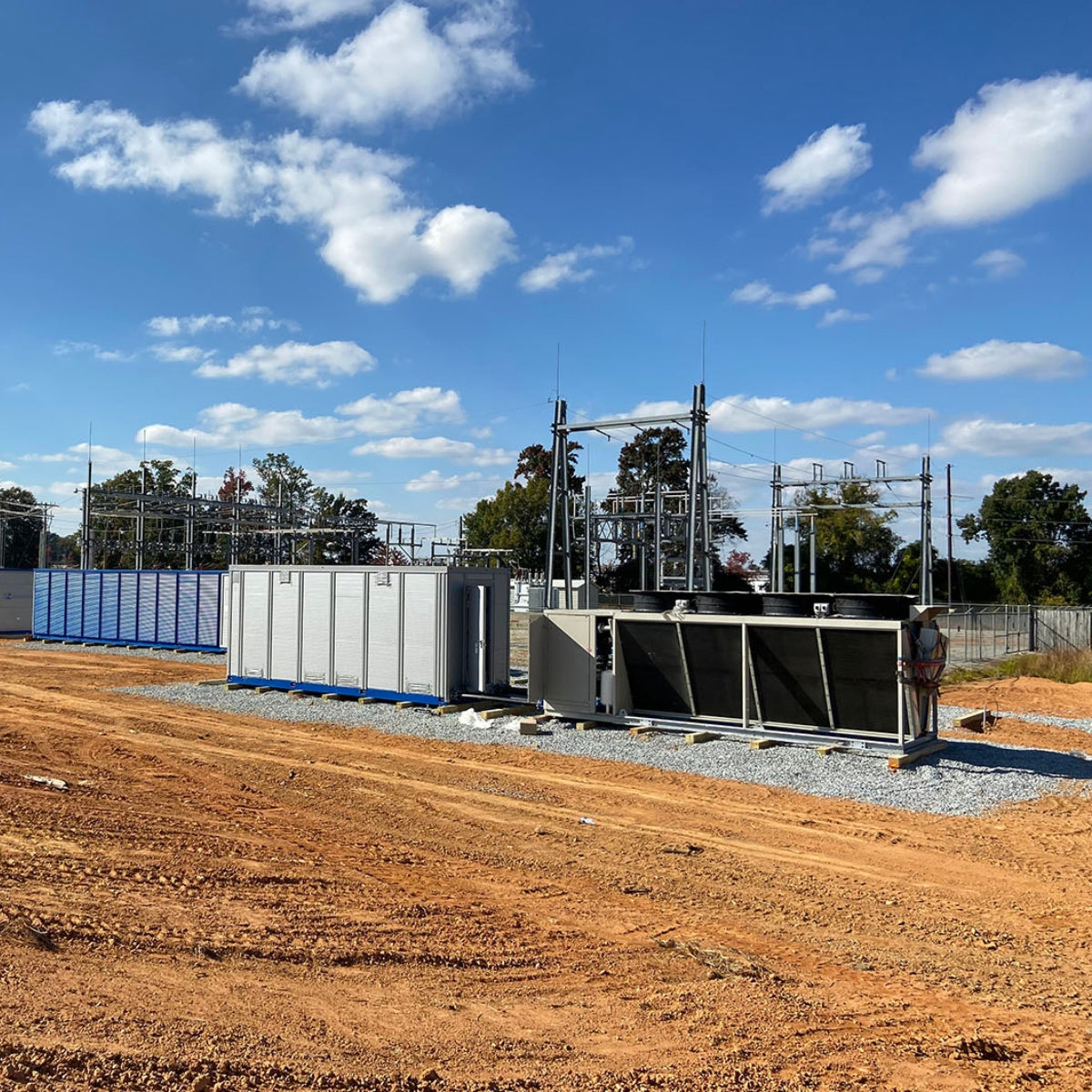 View of cryptocurrency mining containers and cooling equipment at a South Carolina hosting facility with a power substation in the background under a clear sky.